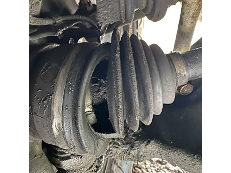 Torn inner CV boot with grease splatter and worn tripod joint tulip tracks showing roller scoring and flat spots causing shudder and clunk under acceleration